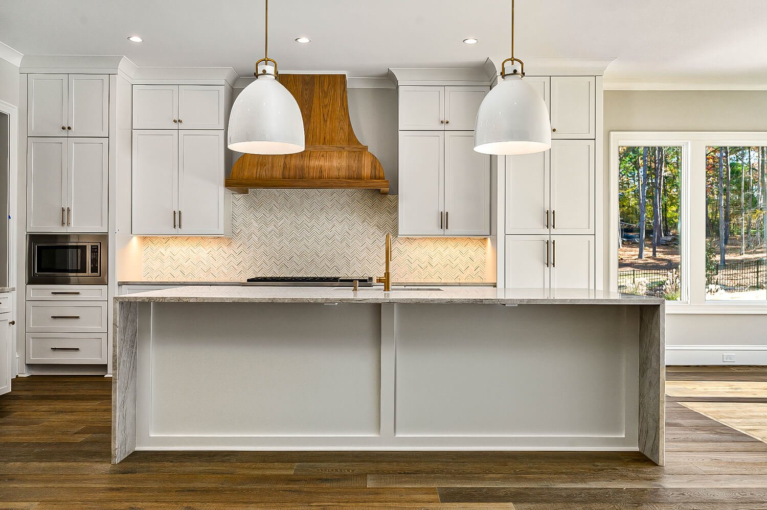 Modern kitchen featuring white cabinets, wood range hood, and herringbone tile, photographed in Raleigh by R. Huggins Media