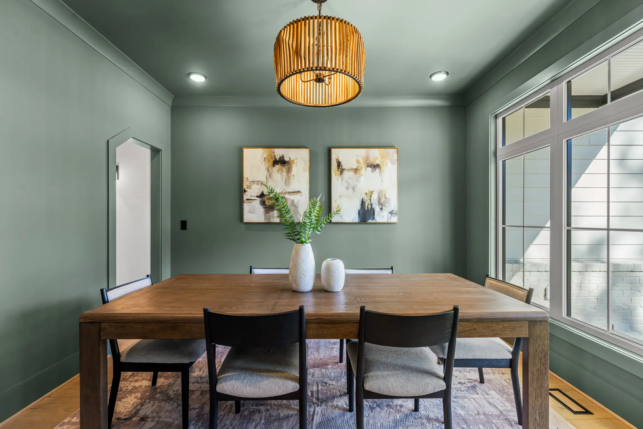 Green dining room with wood table, slatted pendant light and abstract art, Raleigh real estate photography by R. Huggins